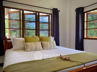 Cozy bedroom with large windows and stylish decor in a serene setting.