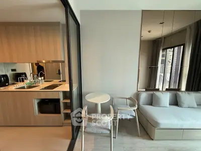 Modern open-layout living room with sleek kitchen and cozy seating area, featuring large windows for natural light.