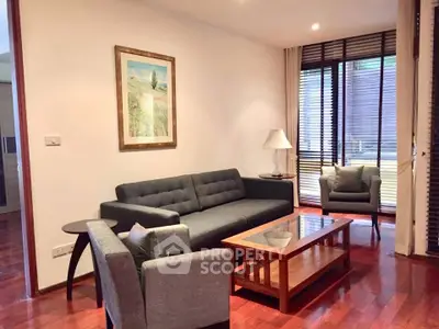 Elegant living room with modern furniture and wooden flooring, featuring a cozy sofa and armchair by large windows.