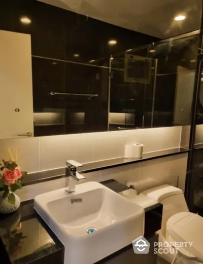 Modern bathroom with sleek black tiles, large mirror, and contemporary fixtures, exuding sophistication and style in a compact space.