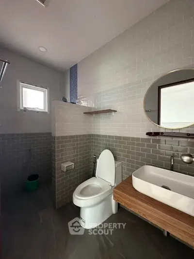 Modern bathroom with sleek design, featuring a stylish sink, round mirror, and contemporary toilet.