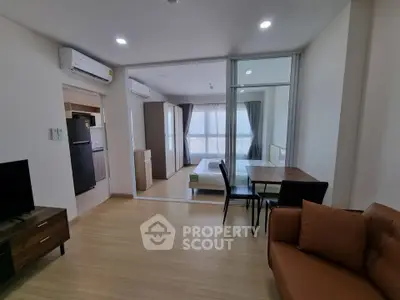 Modern open-plan living room with kitchen and bedroom, featuring sleek furniture and natural light.
