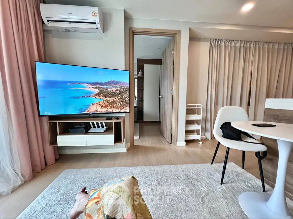 Modern living room with sleek furniture and large TV, featuring a serene beach view on screen.