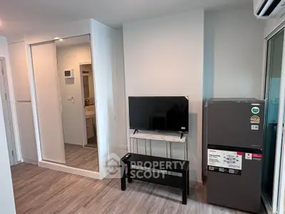 Modern living room with sleek TV setup and stylish refrigerator in a cozy apartment.