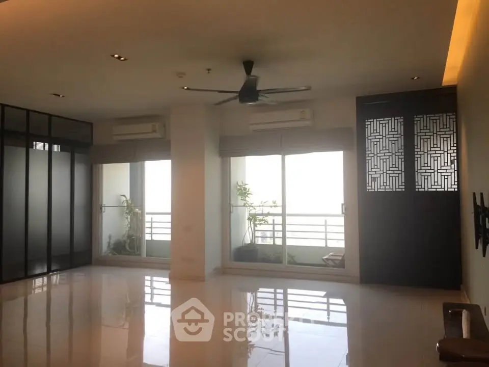 Spacious modern living room with large windows and balcony access, featuring sleek design and ample natural light.