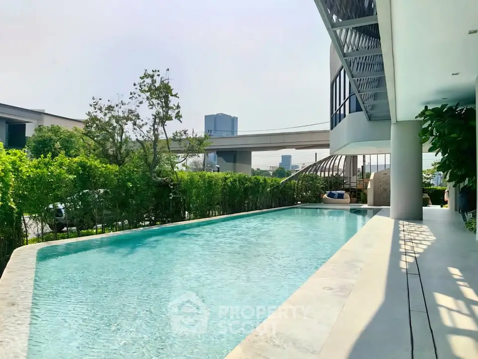 Luxurious modern poolside view with lush greenery and urban backdrop, perfect for relaxation and leisure.