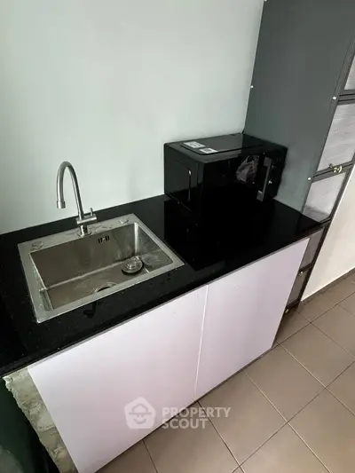 Modern kitchen with sleek black countertop and built-in sink, featuring a compact microwave.