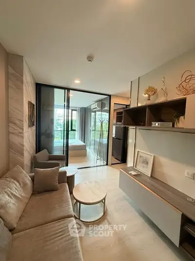 Modern living room with cozy sofa and stylish decor, featuring a view into a chic bedroom through glass doors.