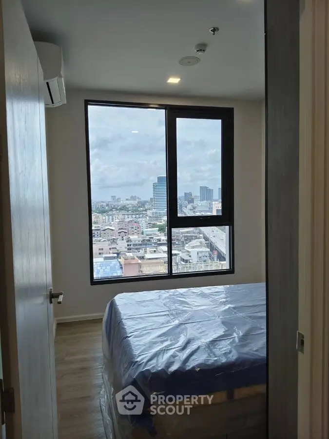 Cozy bedroom with city view, large window, and modern decor in urban apartment.