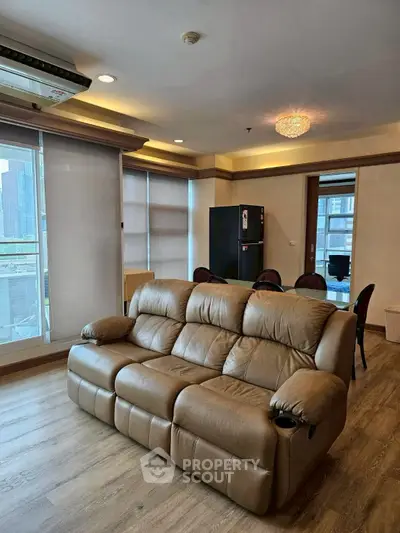 Spacious living room with leather sofa and dining area, featuring large windows and modern lighting.