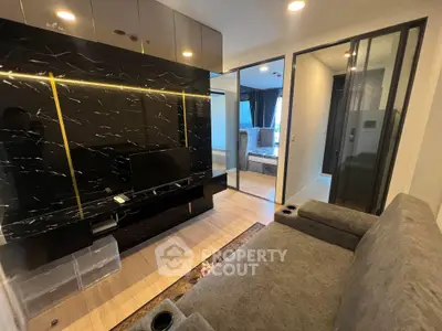 Modern living room with sleek black marble wall and cozy gray sofa, featuring elegant lighting and stylish decor.