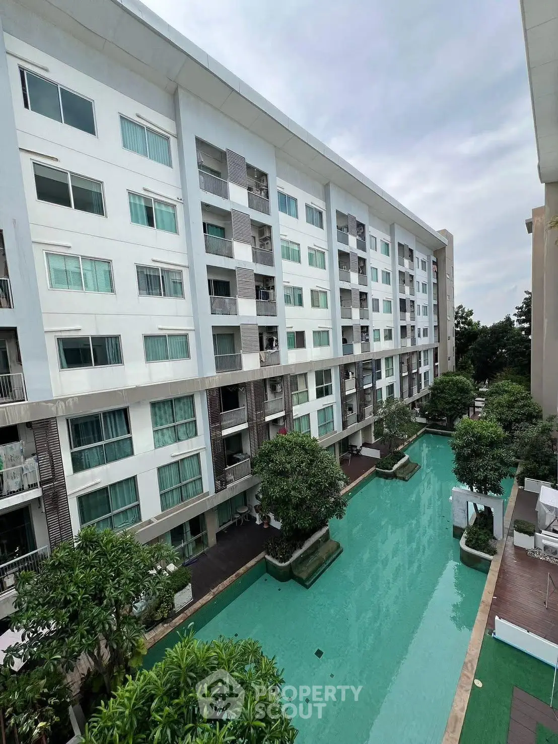 Modern apartment building with pool view and lush greenery, perfect for urban living.