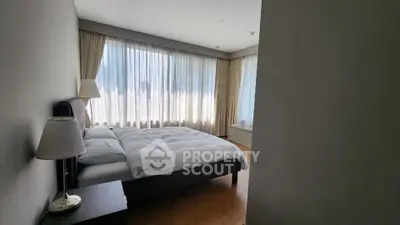 Spacious bedroom with large windows and elegant curtains in modern apartment.