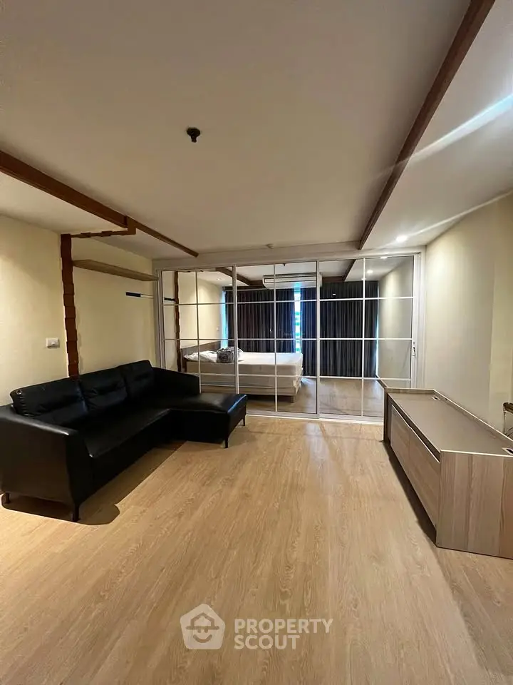 Spacious living room with modern decor and a view into the bedroom through glass doors.