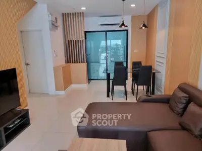 Modern living room with stylish decor and dining area, featuring sleek furniture and large windows.