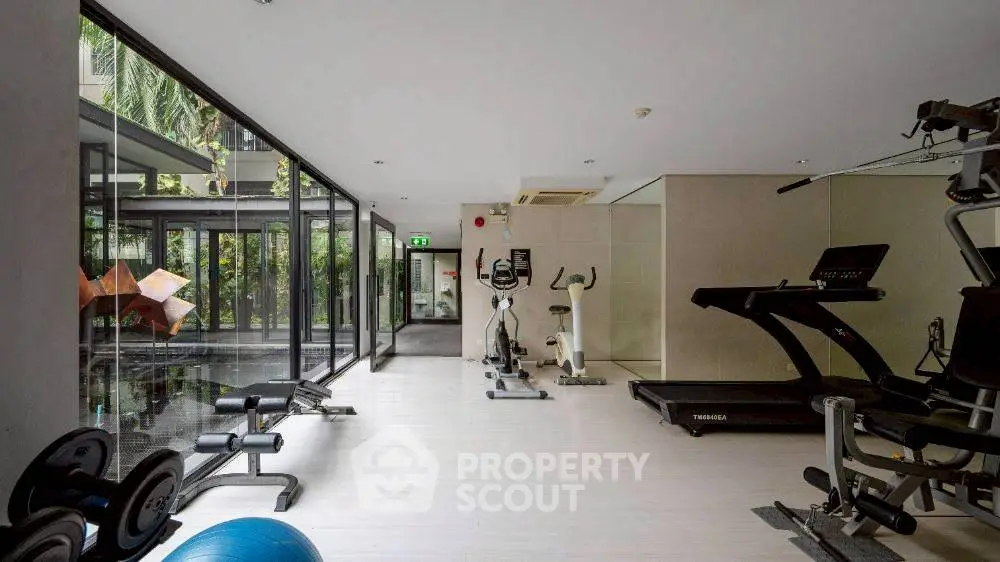 Modern gym with exercise equipment and large windows overlooking greenery.