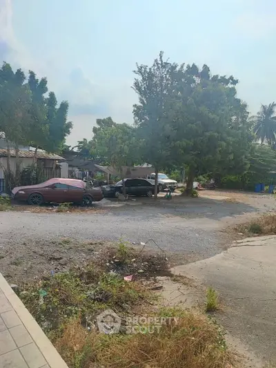 Spacious outdoor parking area with lush greenery and multiple vehicles parked.