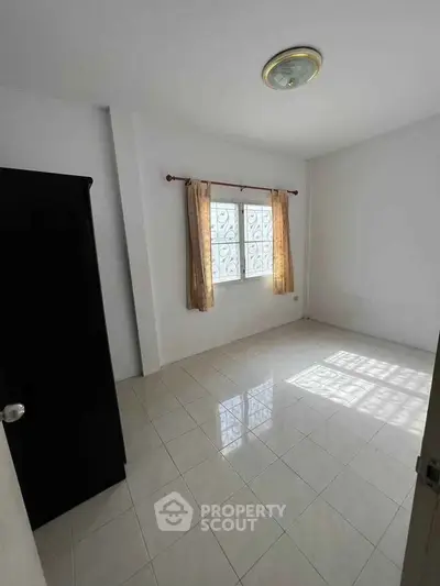 Spacious empty room with tiled floor and window, ideal for customization.