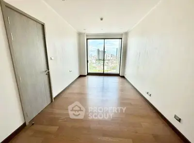 Spacious empty room with wooden flooring and city view through large window.