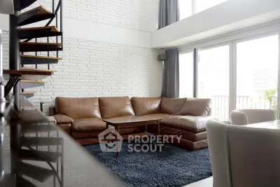Spacious modern living room with leather sofa and spiral staircase, featuring large windows for natural light.