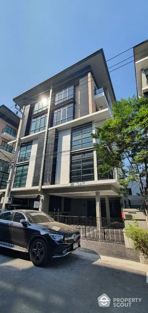 Modern multi-story residential building with a sleek design, large windows, and a secure entrance, nestled in a vibrant neighborhood under a clear blue sky.