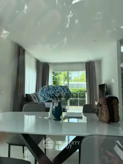 Modern living room with elegant dining area and large windows offering natural light and garden view.