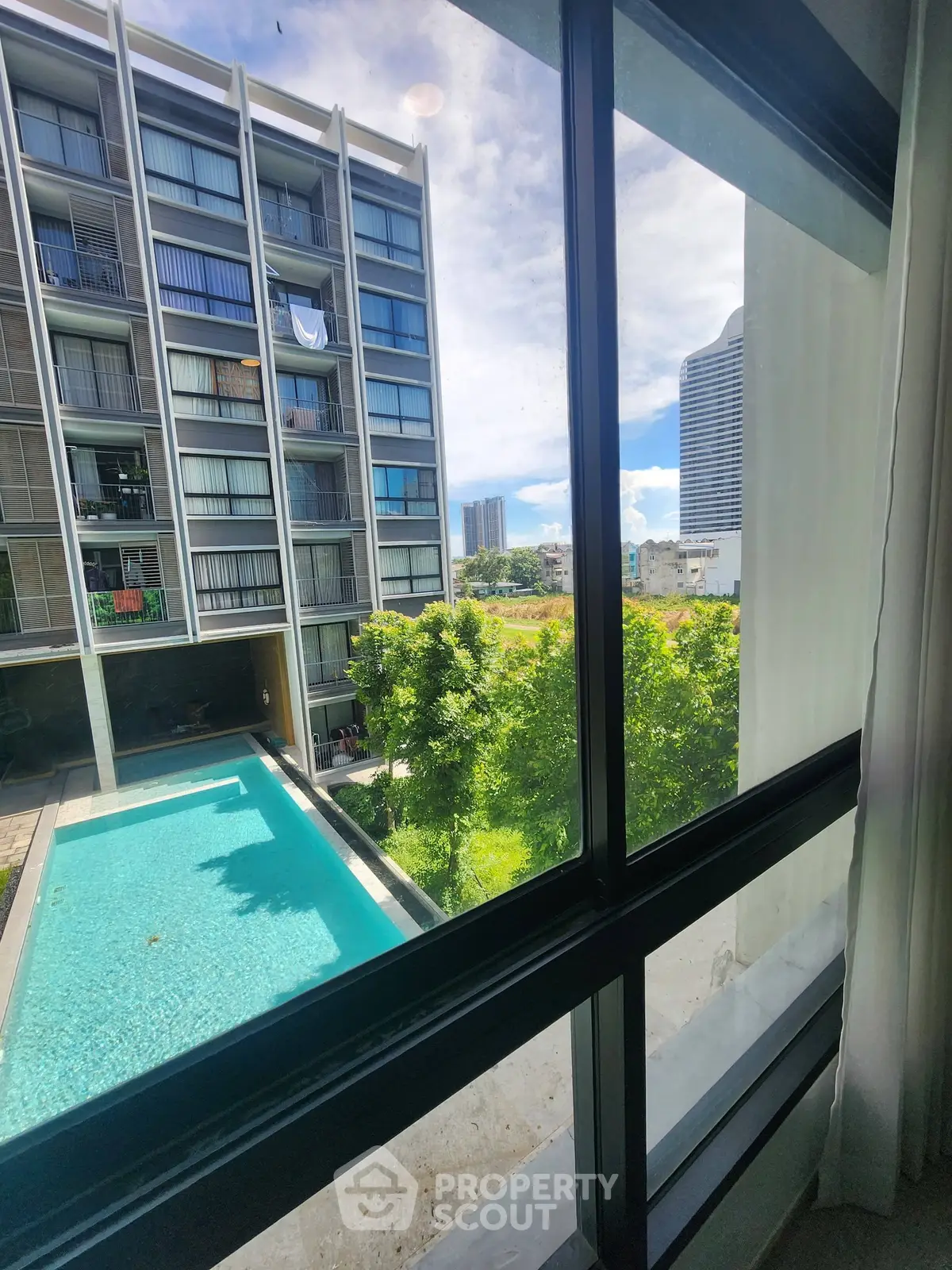 Modern apartment view with pool and cityscape from window, showcasing urban living and luxury amenities.