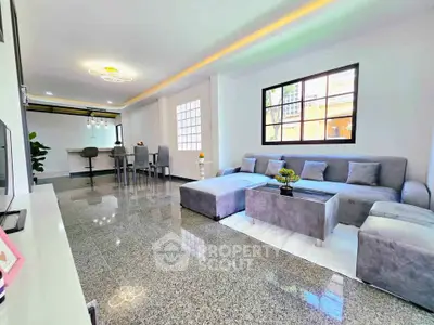 Spacious modern living room with elegant gray sofa and open dining area, featuring sleek lighting and glossy flooring.