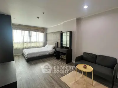 Spacious modern bedroom with cozy seating area and large window for natural light.