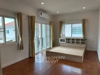 Spacious bedroom with wooden floors and large windows in a modern home.