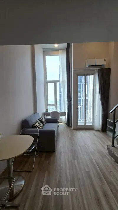 Modern loft-style living room with high ceilings and large windows offering city views.
