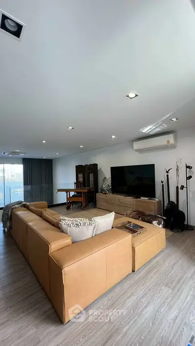 Spacious modern living room with large leather sofa and flat-screen TV, perfect for relaxation and entertainment.