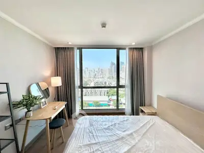 Modern bedroom with city view, featuring a stylish desk and large window for natural light.