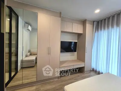 Modern bedroom with built-in wardrobe and TV, featuring sleek design and natural light.