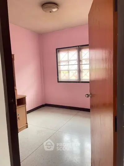 Cozy small bedroom with pink walls and natural light through window.