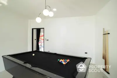 Spacious entertainment room with a sleek black pool table, modern lighting, and a minimalist design, perfect for leisure and social gatherings.