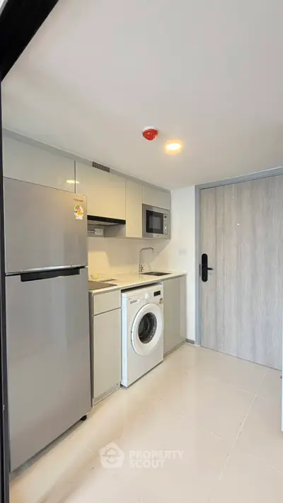 Modern compact kitchen with appliances including fridge, microwave, and washing machine in sleek apartment.