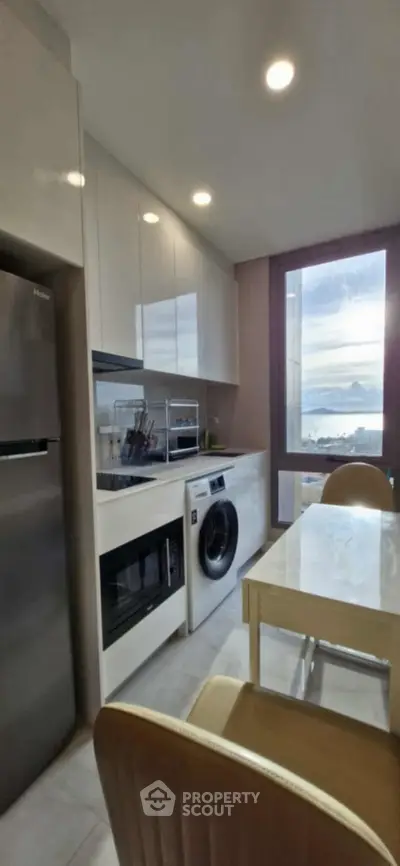 Modern kitchen with appliances and dining area, featuring a washing machine and large window view.