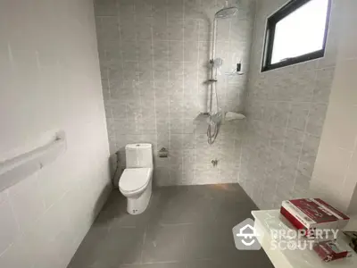 Sleek modern bathroom with wall-mounted toilet, walk-in shower, and stylish grey tiling, complemented by natural light from the frosted window.