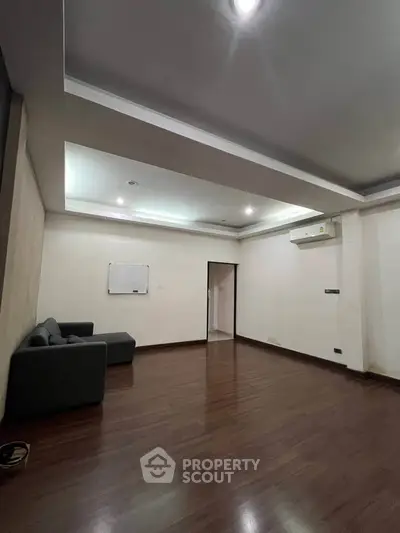 Spacious living room with modern ceiling design and wooden flooring, featuring a cozy sofa and air conditioning.