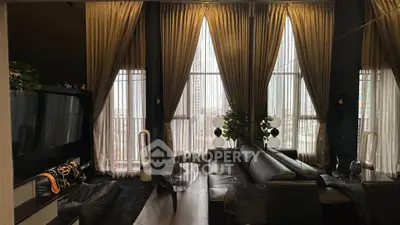 Luxurious living room with high ceilings and elegant drapery, featuring modern black leather furniture.