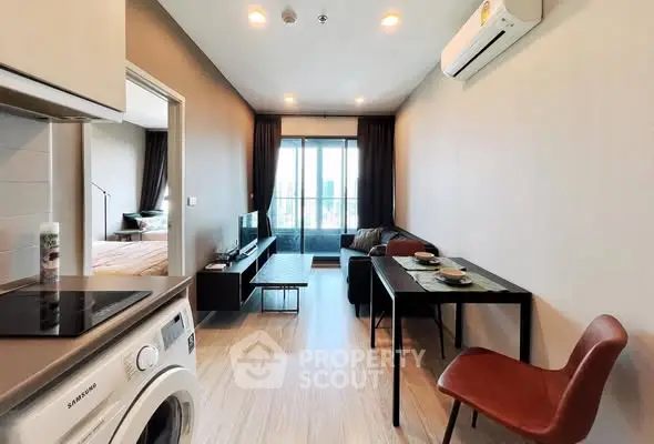Modern living room with open kitchen and city view, featuring sleek furniture and natural lighting.