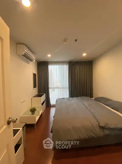 Cozy bedroom with modern furnishings and large window offering natural light.