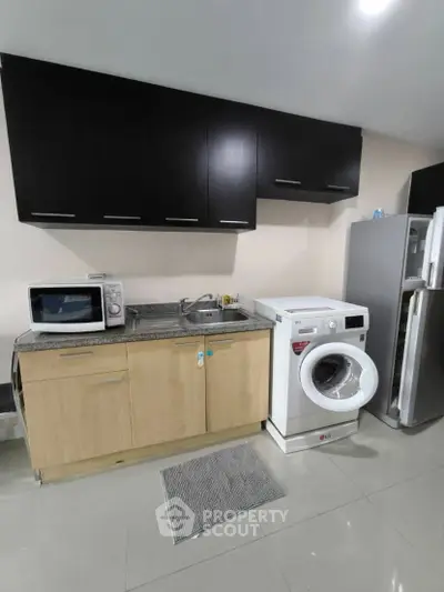 Modern kitchen with sleek cabinets, washing machine, and stainless steel fridge.