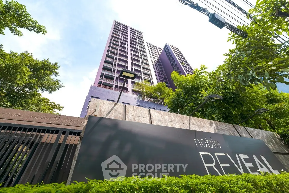 Modern high-rise building with lush greenery and clear blue sky.