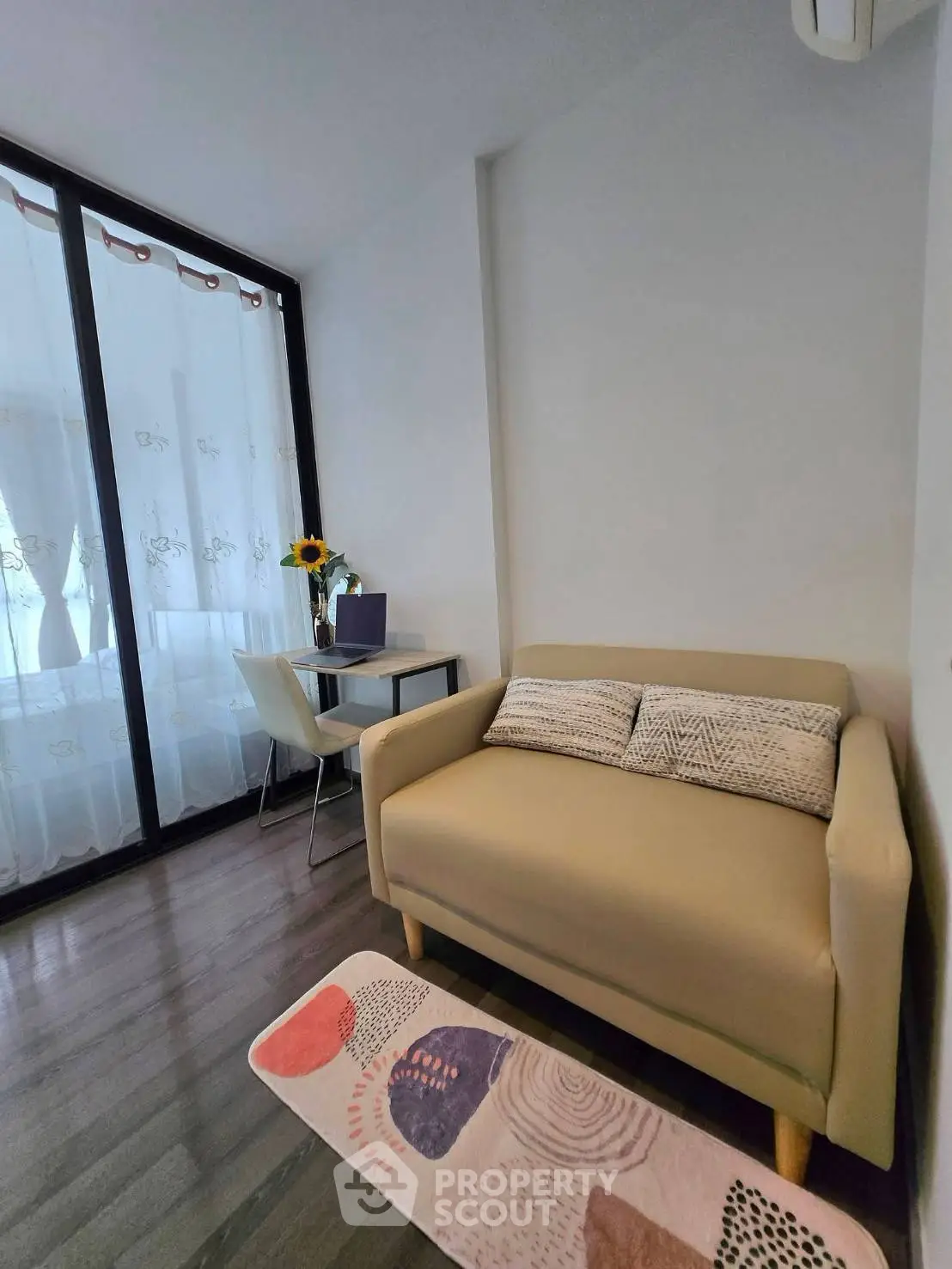 Cozy living room with modern sofa and dining area, featuring large windows and stylish decor.
