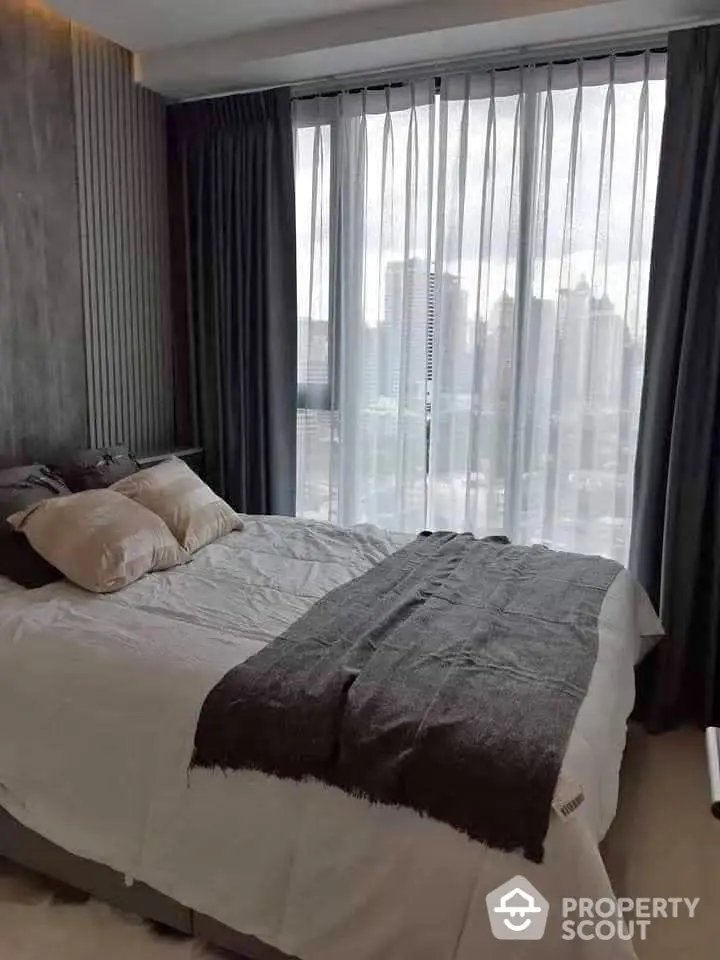 Modern bedroom with city view and elegant decor, featuring large windows and stylish curtains.