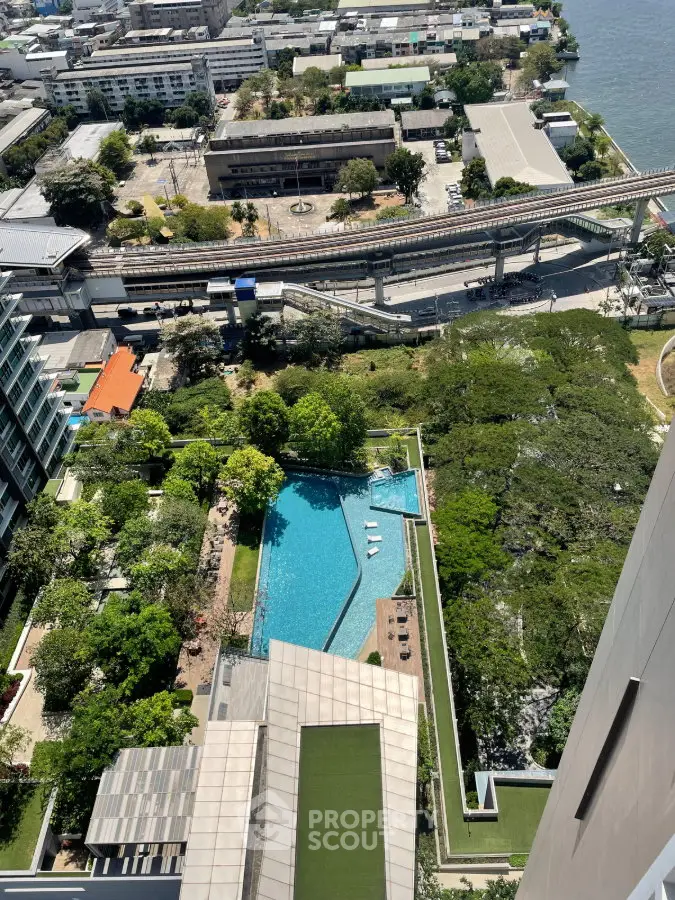 Stunning aerial view of luxury condominium with pool and lush greenery, overlooking cityscape and river.