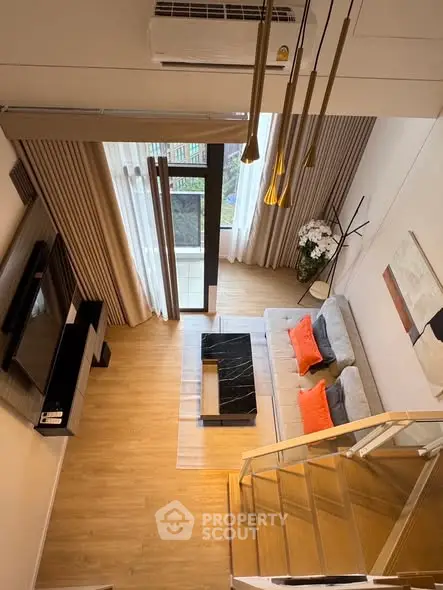 Modern living room with stylish decor, large windows, and elegant staircase view from above.