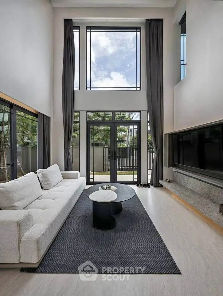 Luxurious modern living room with high ceilings and large windows offering natural light and garden view.